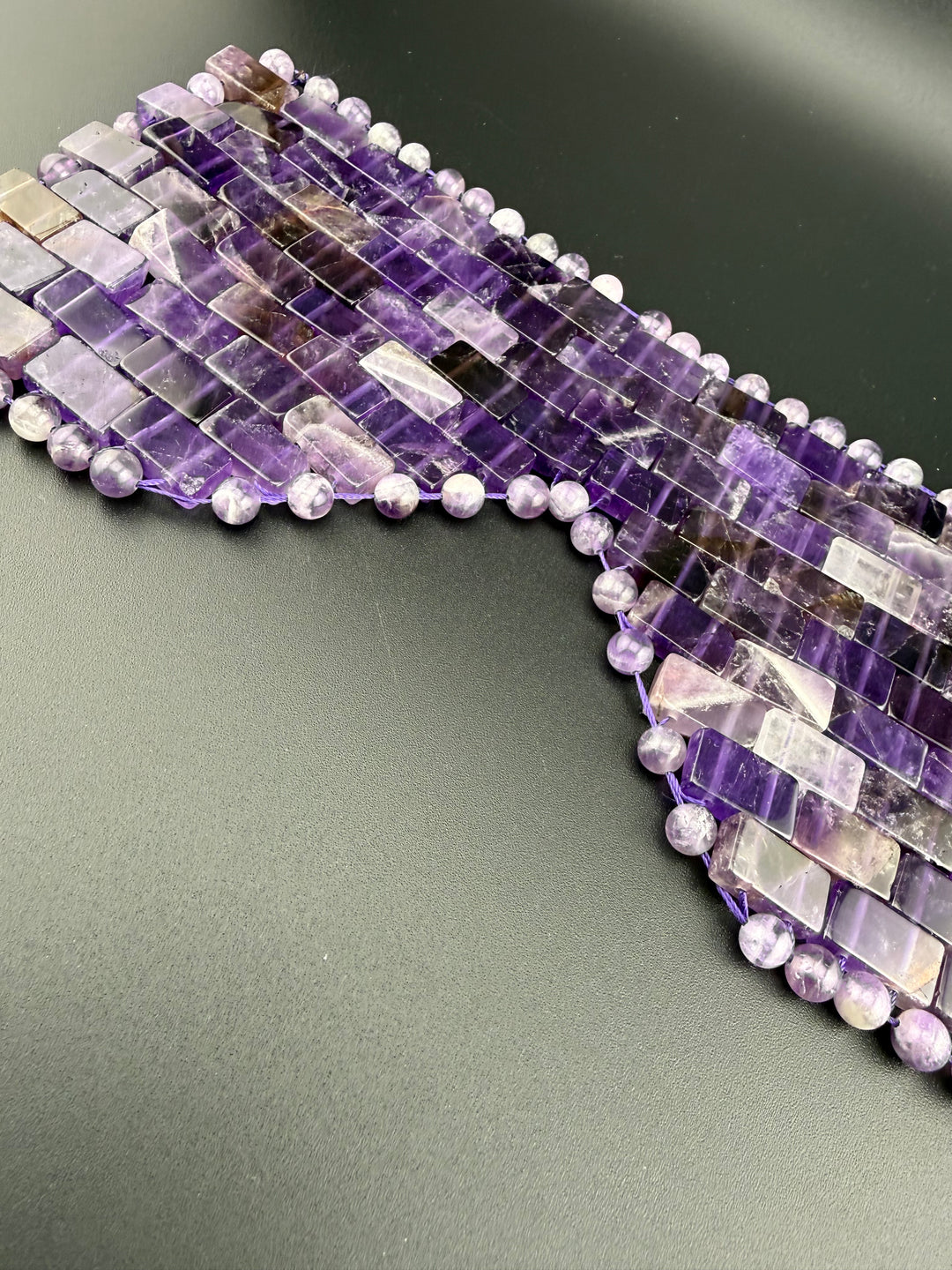 Natural amethyst crystal eye mask with polished gemstone tiles and beads displayed on a dark background for relaxation, meditation, and spa wellness.