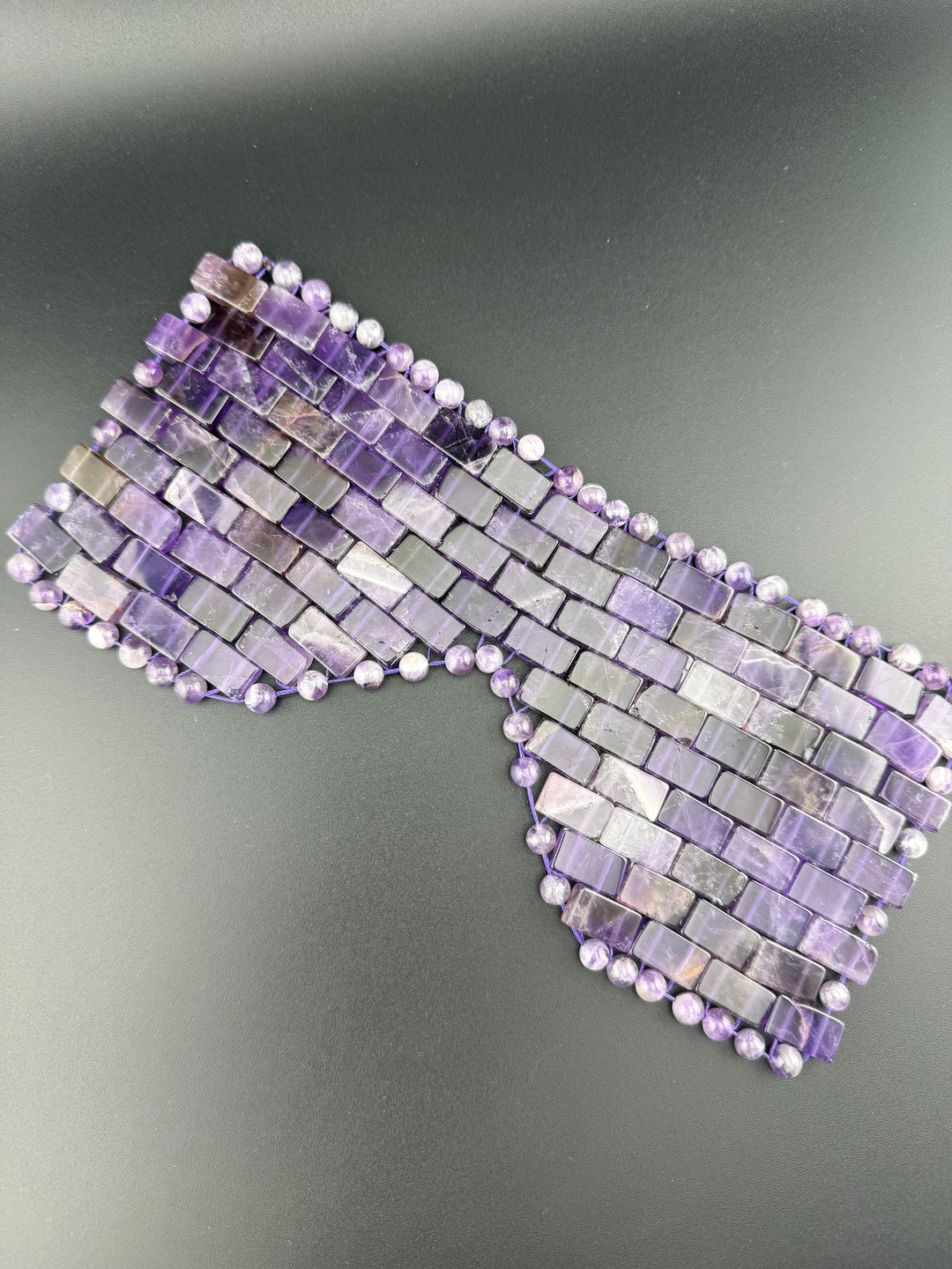 Natural amethyst crystal eye mask with polished gemstone beads displayed on a dark background for relaxation, meditation, cooling eye therapy, and spa wellness.