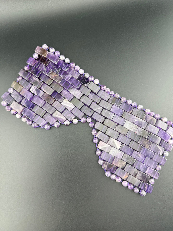 Natural amethyst crystal eye mask with polished gemstone beads displayed on a dark background for relaxation, meditation, cooling eye therapy, and spa wellness.