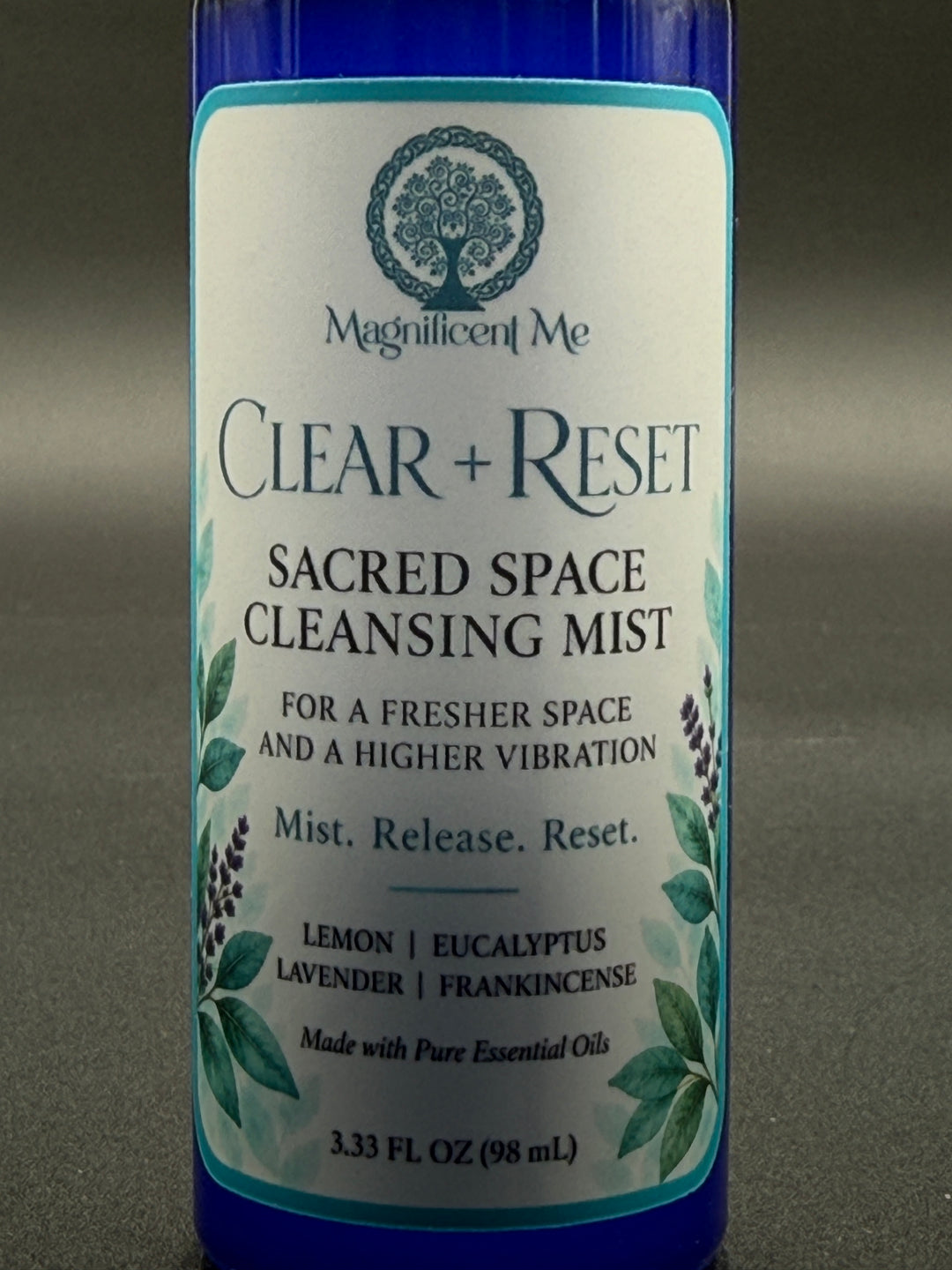 Close-up of Clear + Reset Sacred Space Cleansing Mist label showing the Magnificent Me logo and lemon, eucalyptus, lavender and frankincense essential oil blend.