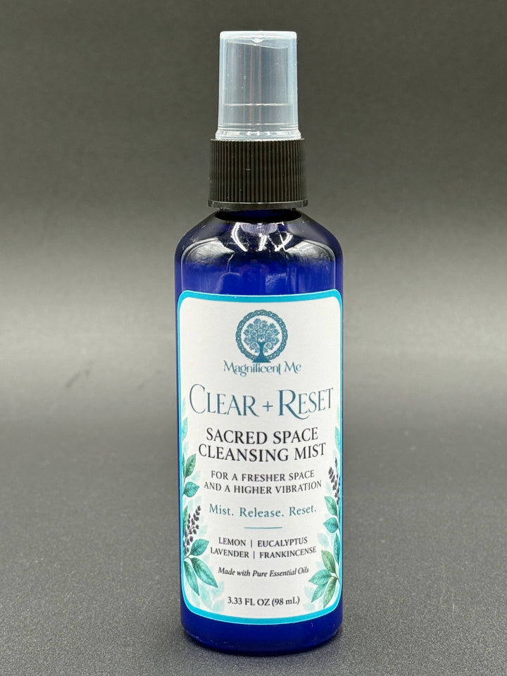 Magnificent Me Clear + Reset essential oil room spray in a cobalt-blue bottle with botanical label, featuring lemon, eucalyptus, lavender and frankincense.
