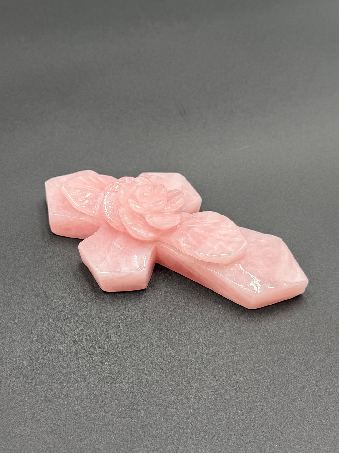 Detailed view of a natural pink rose quartz cross showing the smooth polished crystal surface, subtle white inclusions, and sculpted rose petals.