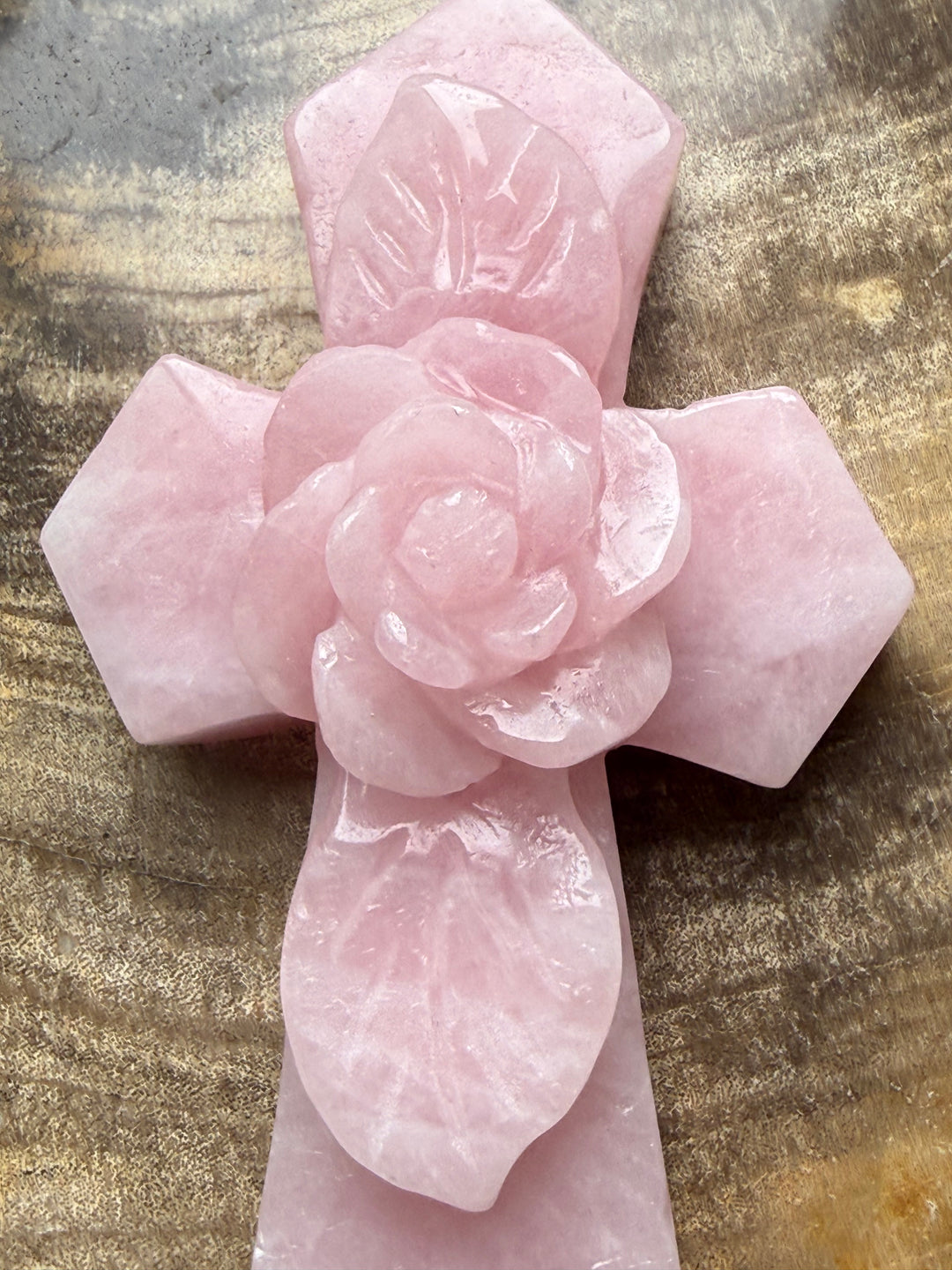 Close-up of a delicate carved rose flower at the center of a polished pink rose quartz crystal cross, showcasing its detailed floral design.