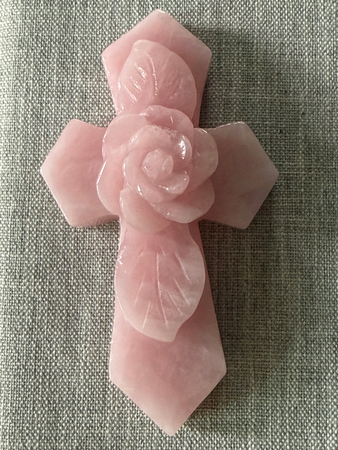 Large rose quartz crystal cross with carved rose centerpiece displayed as a decorative accent for a meditation altar, prayer space, or sacred home.