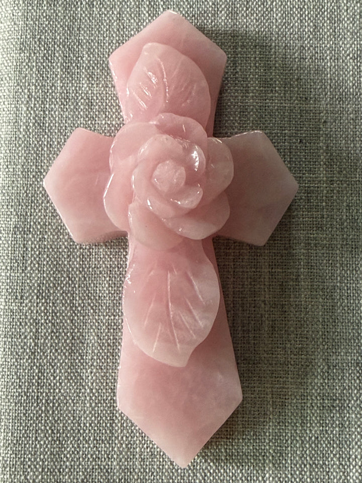 Large rose quartz crystal cross with carved rose centerpiece displayed as a decorative accent for a meditation altar, prayer space, or sacred home.