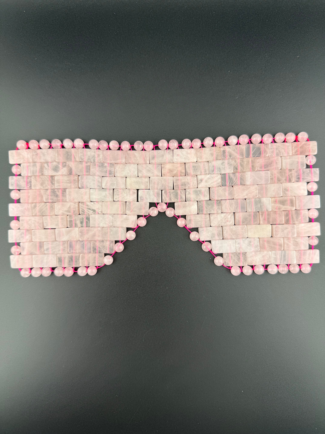 Natural rose quartz crystal eye mask displayed on a dark background for cooling relaxation, meditation, spa wellness, and luxury self-care rituals.